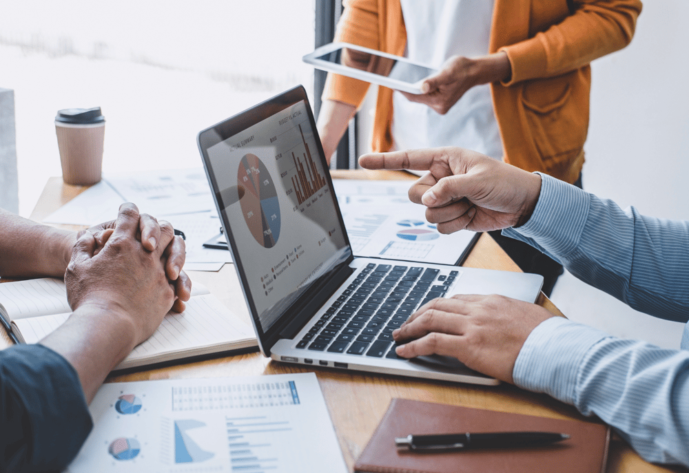 A B2B marketer pointing out conversion statistics on their laptop to fellow team members, representing the benefits of undertaking conversion rate optimisation best practices.