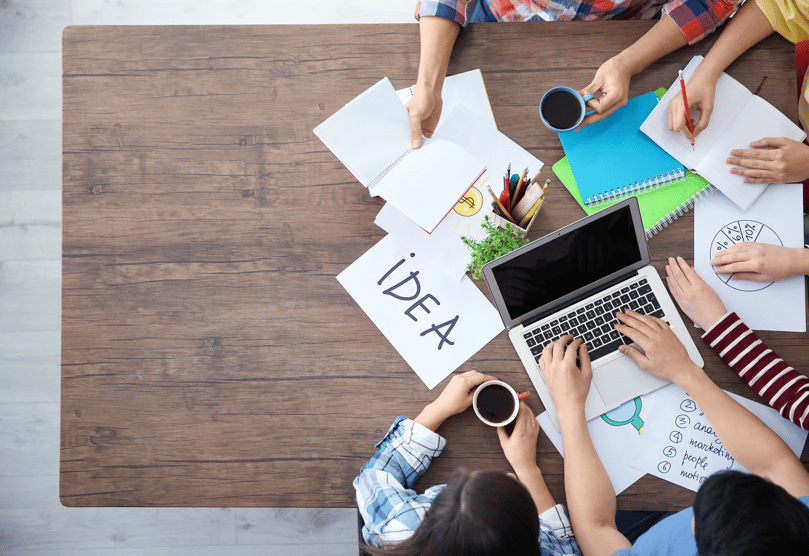 A birds eye view of a marketing team and SEO and content agency working together on content ideas with laptops, paper and notebooks--png