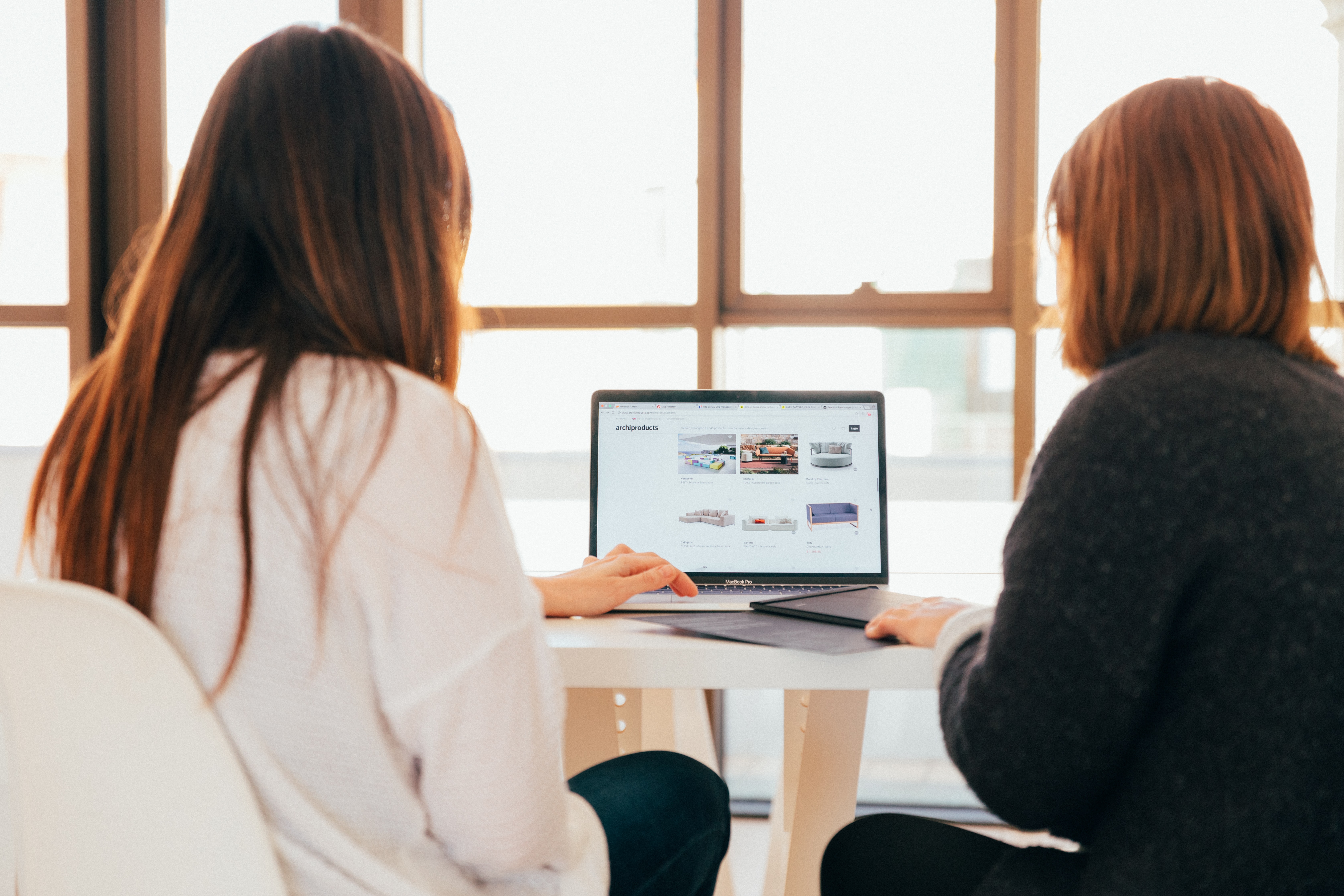 Two women looking at laptop with a webpage of images which helps their b2b content marketing strategy