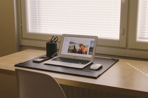 Laptop on a desk in front of a window and next to a pot of stationery to represent website design seo mistakes